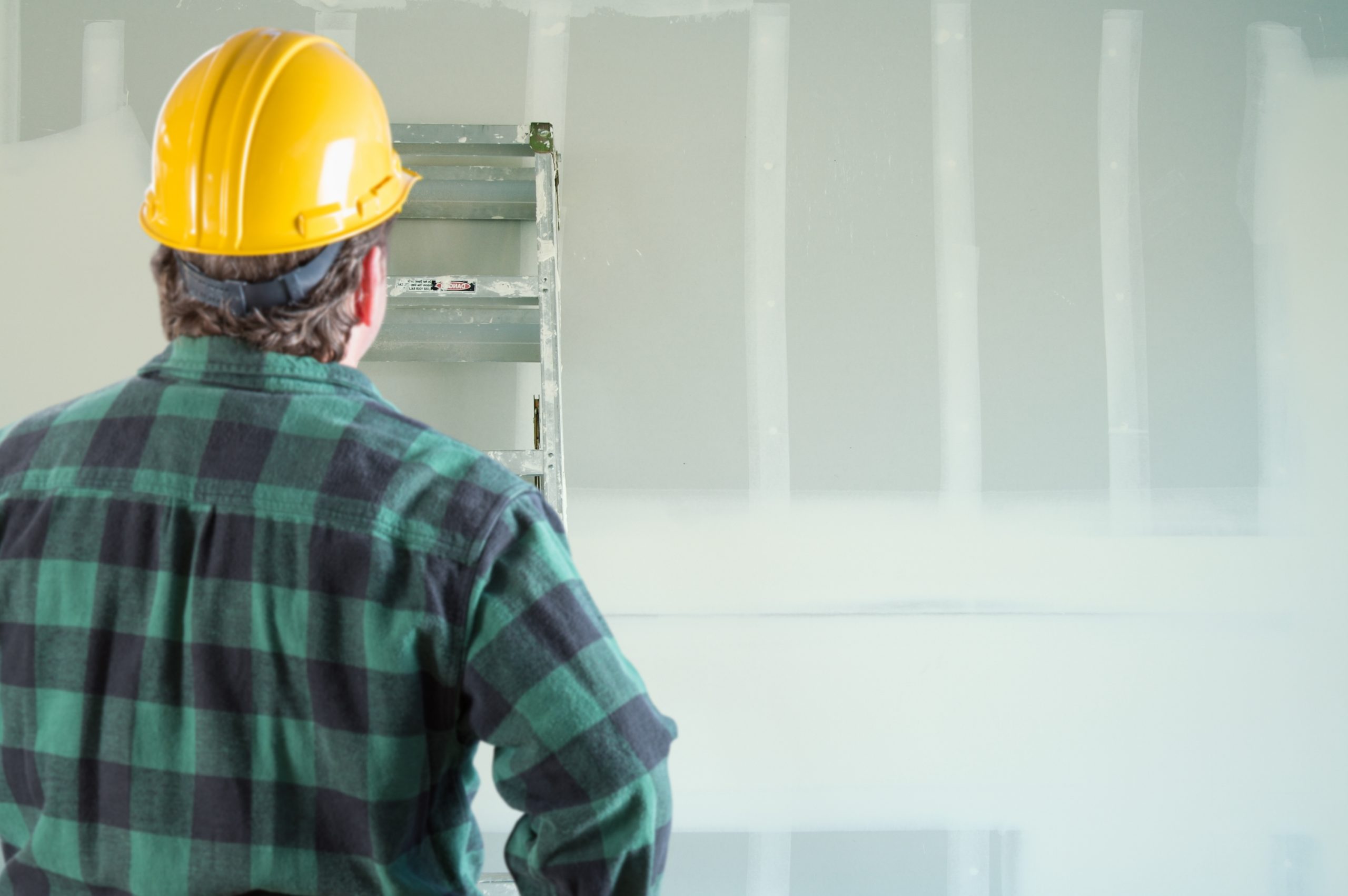 construction worker wearing a black and green plaid shirt and a yellow hard hat looking at interior building
