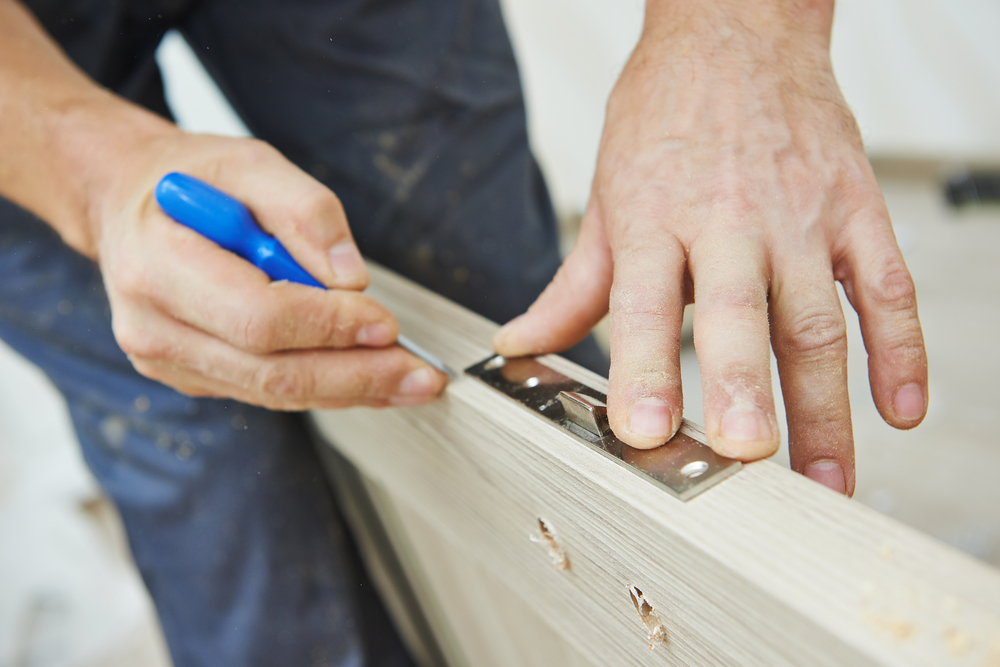 Close-up,Carpenter,Hands,With,Doorlock,During,Lock,Process,Installation,Into carpentry work on a door