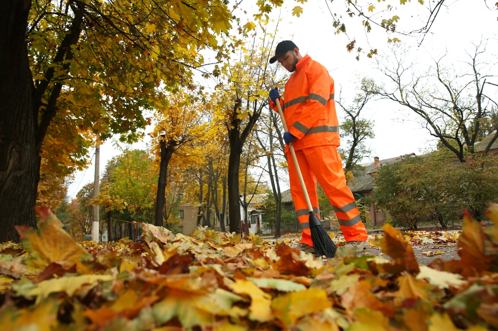 janitor raking up the leaves outside a property